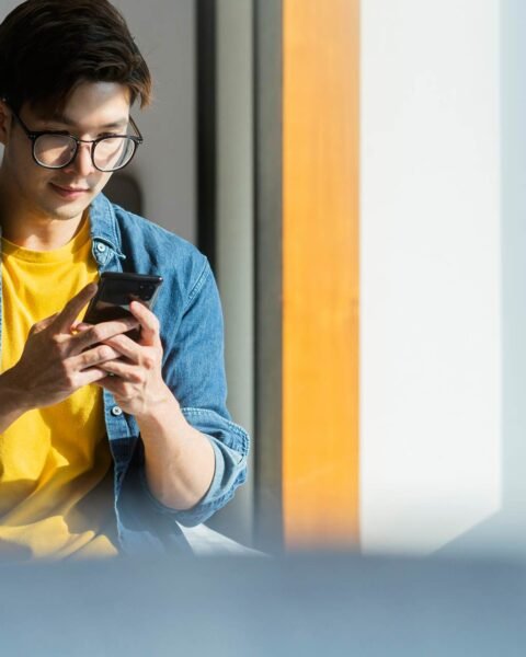 young-adult-asian-traveller-male-casual-cloth-with-jean-jacket-hand-use-smartphone-conversation-checking-schedule-trip-white-soft-bed-with-luggage-bagpack-vacation-weekend-travel-concept