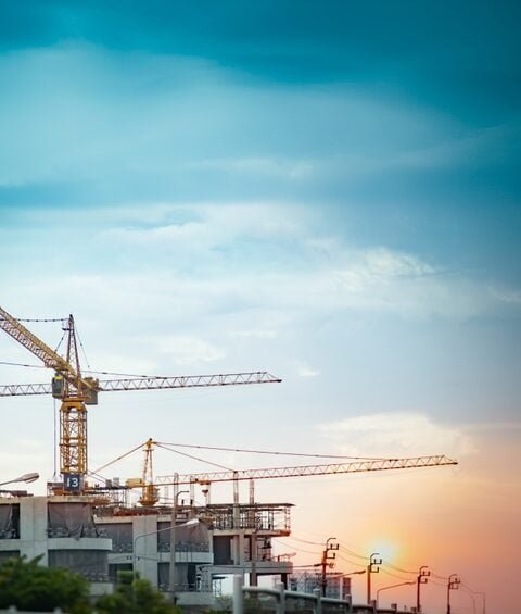 Sunset casts a warm glow on construction cranes at a site in Cambodia, highlighting the country's growth and development, also the improved Cambodian Construction Regulations.