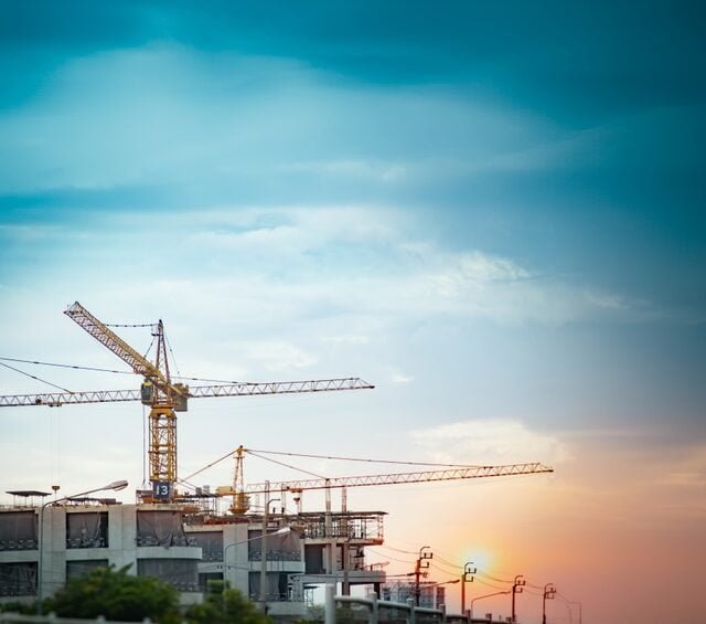 Sunset casts a warm glow on construction cranes at a site in Cambodia, highlighting the country's growth and development, also the improved Cambodian Construction Regulations.