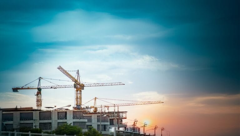 Sunset casts a warm glow on construction cranes at a site in Cambodia, highlighting the country's growth and development, also the improved Cambodian Construction Regulations.