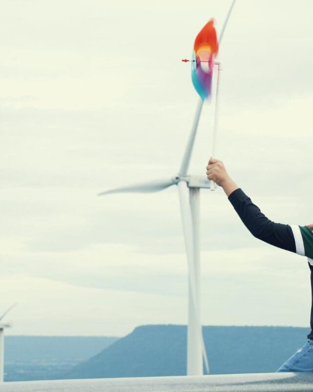 Cambodia Renewable Energy in Construction: Two people sitting by wind turbines holding a colorful pinwheel.