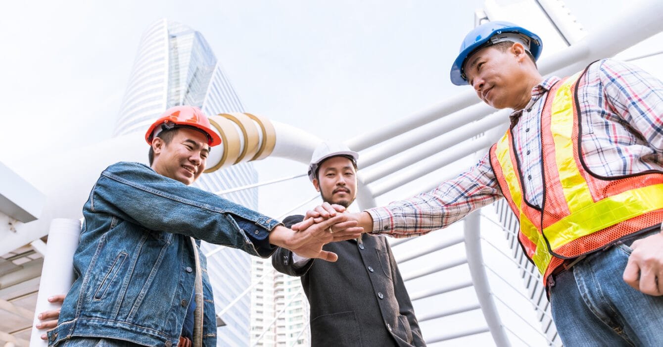 Cambodia Construction Workforce Trends: Three construction workers in hard hats doing a team hand stack outdoors.