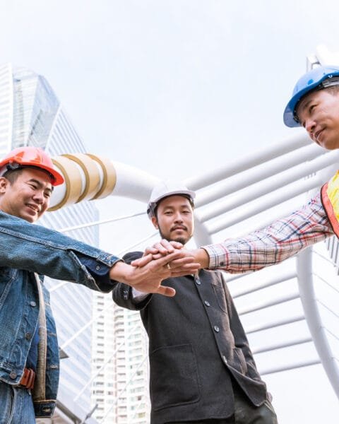 Cambodia Construction Workforce Trends: Three construction workers in hard hats doing a team hand stack outdoors.