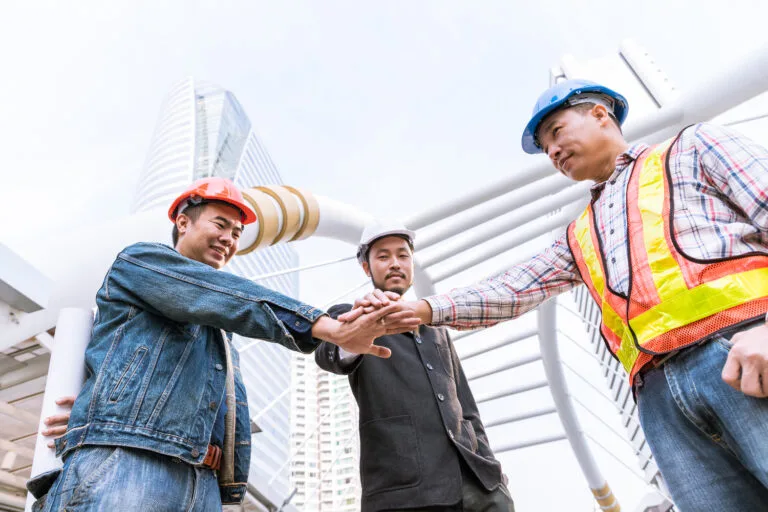 Cambodia Construction Workforce Trends: Three construction workers in hard hats doing a team hand stack outdoors.
