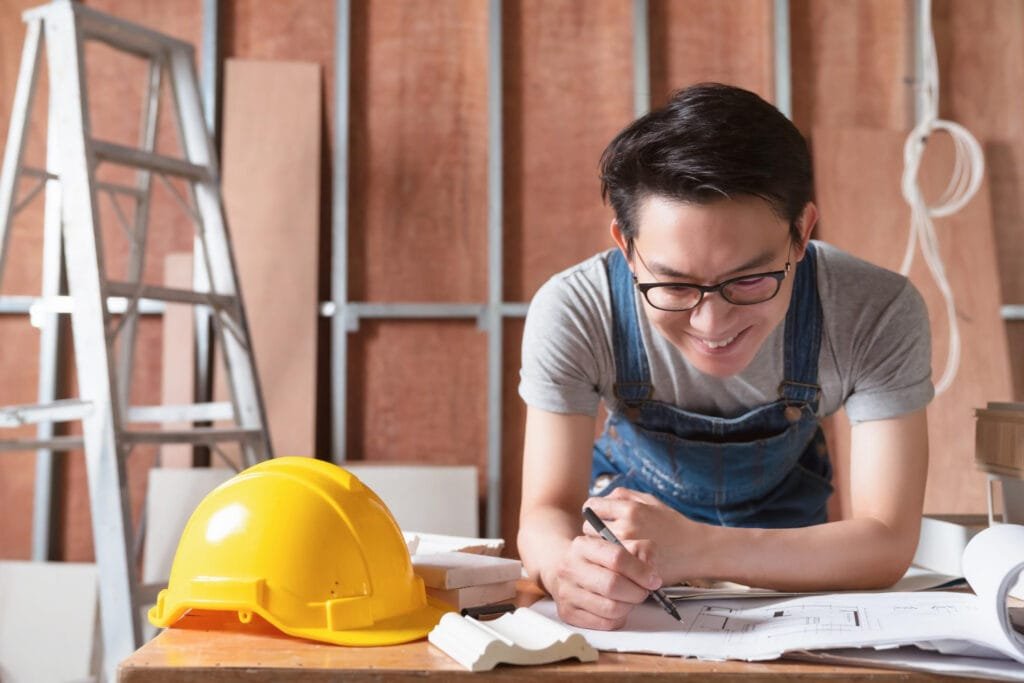 Cambodia Construction Workforce Trends: Person in overalls working on architectural plans with a hard hat on the table.