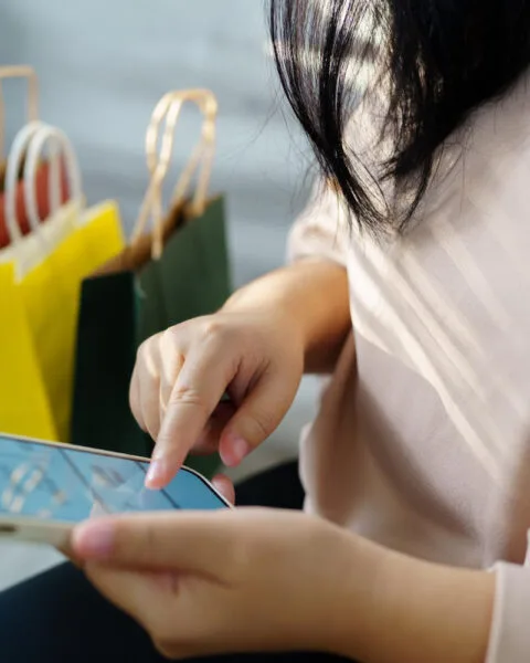 A woman shopping online on her smartphone, with colorful shopping bags in the background, representing Cambodia Consumer Market Trends.