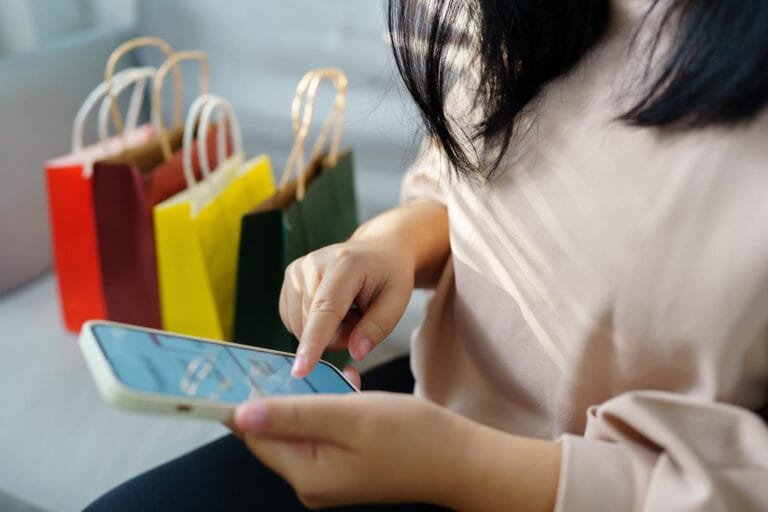 A woman shopping online on her smartphone, with colorful shopping bags in the background, representing Cambodia Consumer Market Trends.