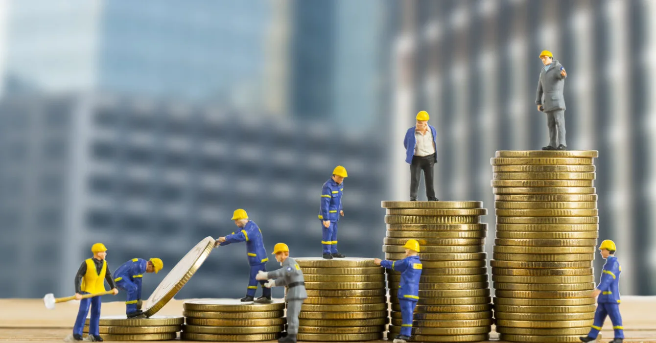 Cambodia Construction Financing Challenges: Miniature construction workers stack coins, symbolizing teamwork and growth in finance or investment against a city backdrop.