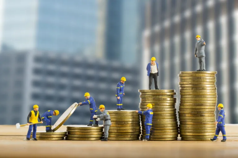 Cambodia Construction Financing Challenges: Miniature construction workers stack coins, symbolizing teamwork and growth in finance or investment against a city backdrop.