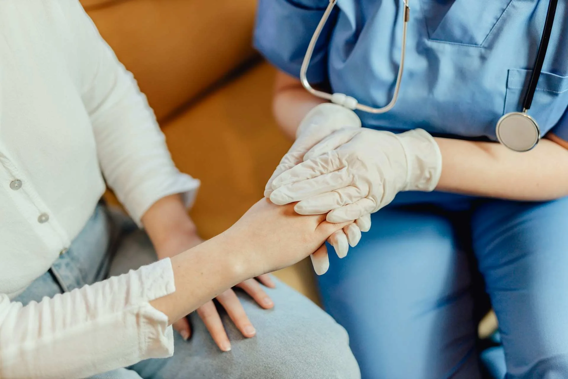 Cambodia Healthcare Market Expansion: A healthcare professional in gloves gently holds a patient's hand, offering comfort during a consultation.