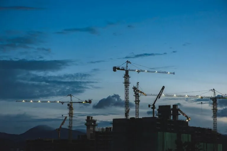 Cambodia Construction Industry Growth: Silhouettes of multiple construction cranes against a twilight sky, with clouds and distant mountains in the background.