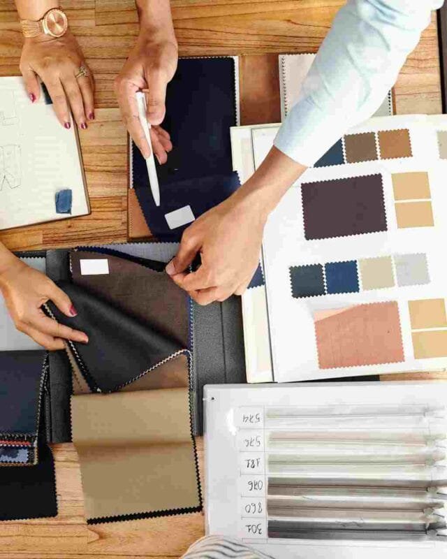 Cambodia Textile Export Strategy: A collaborative workspace featuring hands choosing fabric swatches and reviewing design notes, with tools and sketches scattered on a table.