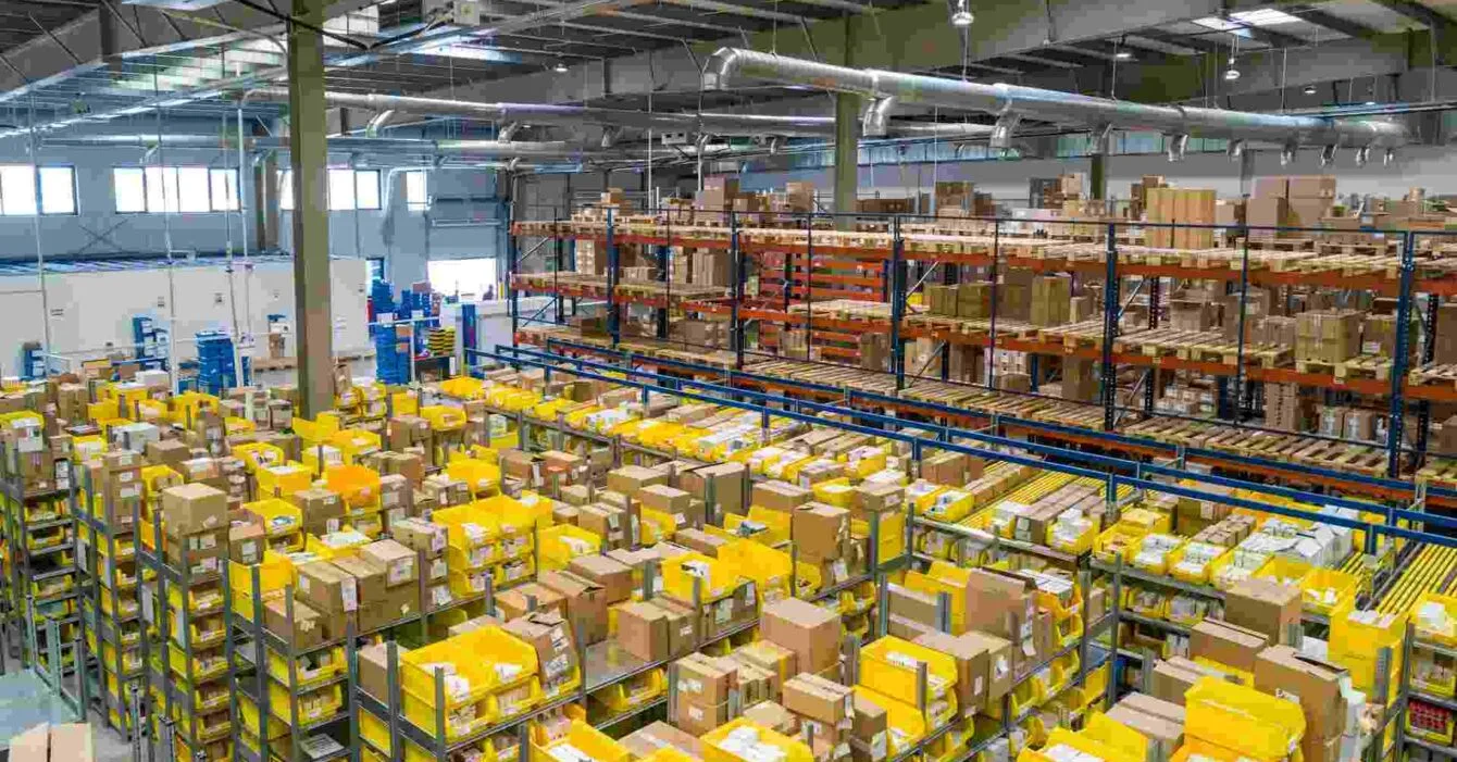 adrian-sulyok-sczNLg6rrhQ-unsplash Cambodia Logistics Infrastructure Development: A spacious warehouse filled with yellow bins and stacked boxes on shelves, highlighting an organized distribution environment.