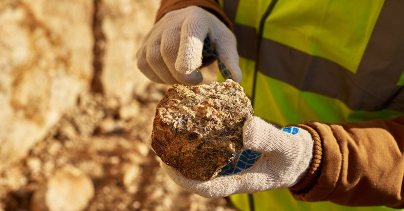 Cambodia Mining Regulatory Reform: A miner in a safety vest examines a rock, showcasing its texture, while outdoors in a mineral-rich environment.
