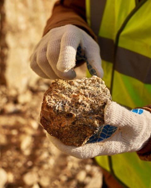 Cambodia Mining Regulatory Reform: A miner in a safety vest examines a rock, showcasing its texture, while outdoors in a mineral-rich environment.