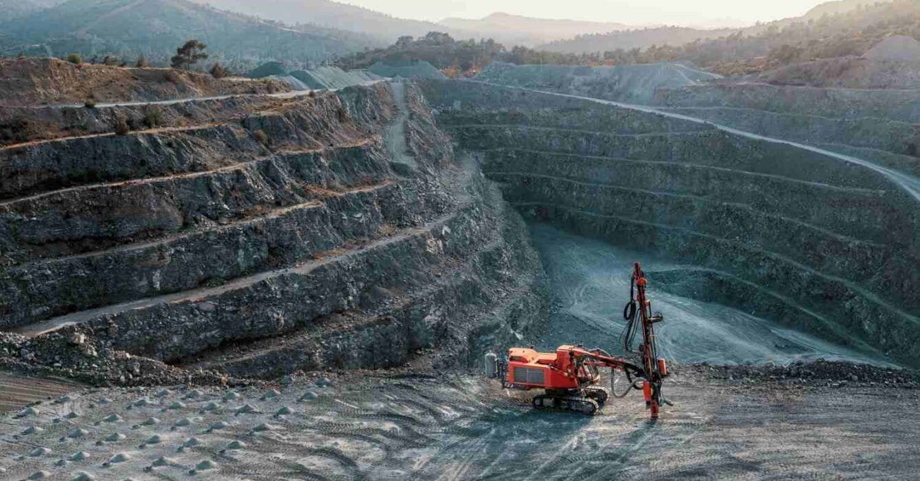 Cambodia Mining Sector Outlook: A quarry scene featuring a red drilling machine on a rocky surface, surrounded by steep, tiered rock formations under a dusky sky.