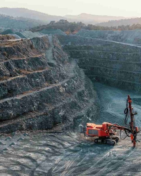 Cambodia Mining Sector Outlook: A quarry scene featuring a red drilling machine on a rocky surface, surrounded by steep, tiered rock formations under a dusky sky.
