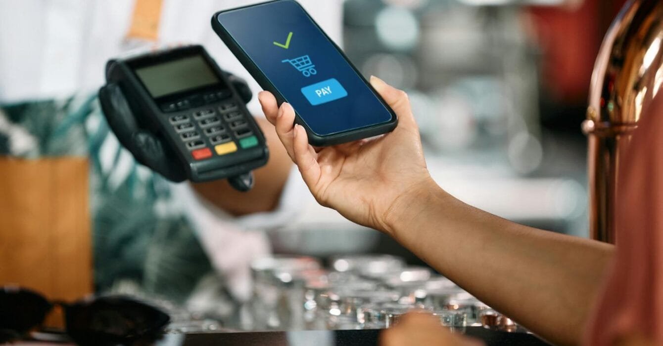 Cambodia Mobile Payments Surge: A customer using a smartphone for contactless payment at a checkout counter, with a card reader in the foreground.