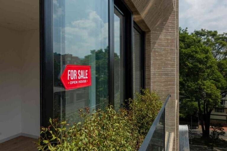 Cambodia Property Market 2025: A bright red "For Sale" sign hangs on a modern window, with lush greenery visible outside and clear skies above.