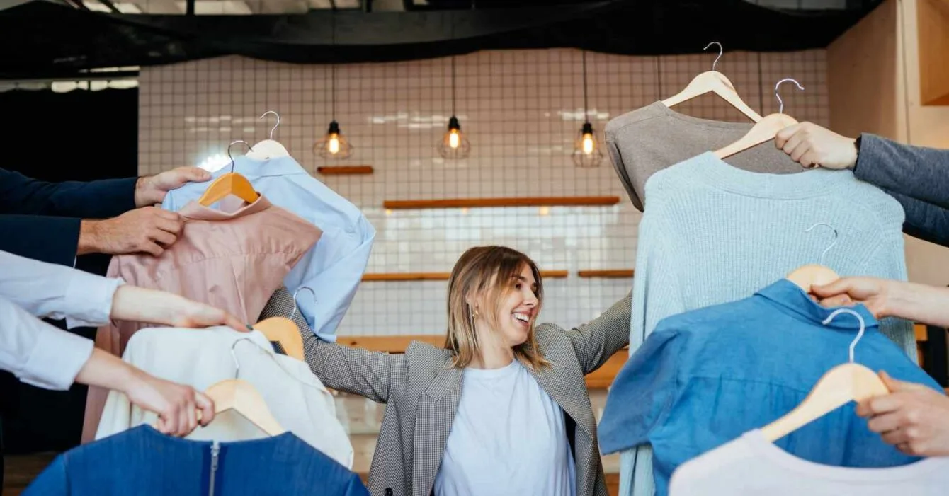 Cambodia Garment Export Diversifies: A woman surrounded by multiple hands holding various stylish clothing items in a modern retail setting.