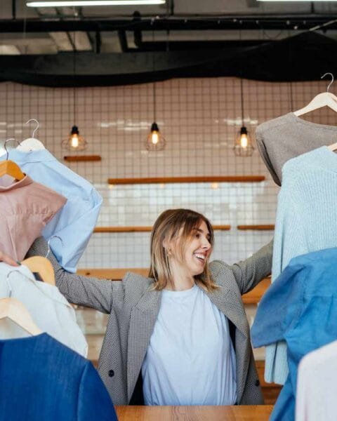 Cambodia Garment Export Diversifies: A woman surrounded by multiple hands holding various stylish clothing items in a modern retail setting.