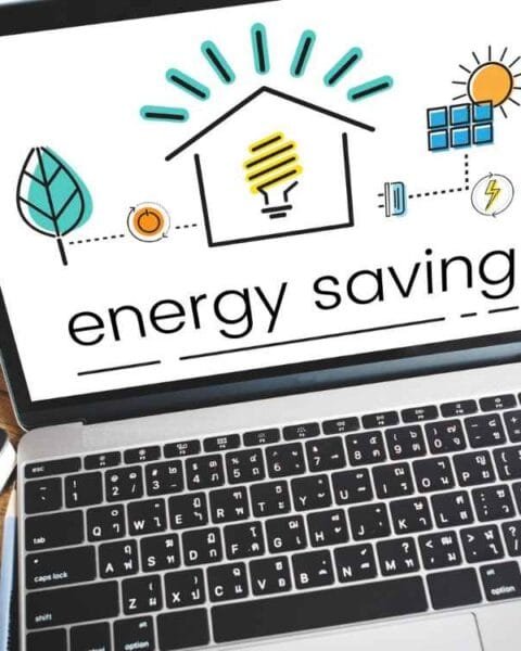 Cambodia Energy Deal Watch: A laptop displays an energy saving graphic with icons of a house, light bulb, sun, and leaf, alongside a cup of coffee and a notebook.