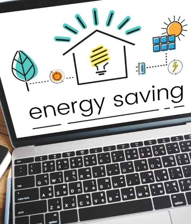 132216 Cambodia Energy Deal Watch: A laptop displays an energy saving graphic with icons of a house, light bulb, sun, and leaf, alongside a cup of coffee and a notebook.