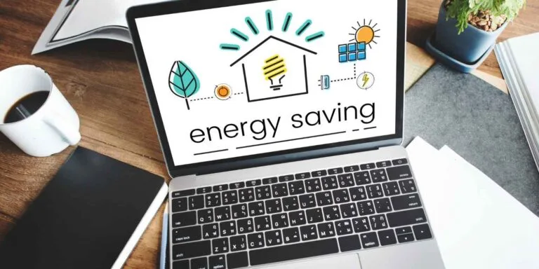 Cambodia Energy Deal Watch: A laptop displays an energy saving graphic with icons of a house, light bulb, sun, and leaf, alongside a cup of coffee and a notebook.